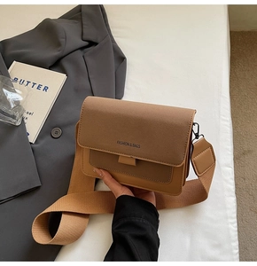 Close-up of minimalist brown crossbody bag with wide woven strap and fashion text detail