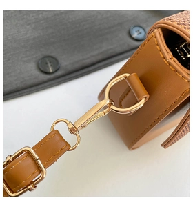 Detail of gold lobster clasp on brown leather saddle bag with luxury monogram pattern