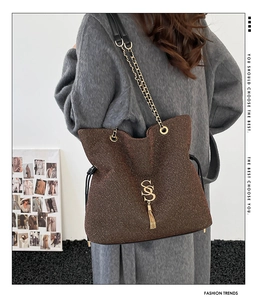 Detail of brown tweed tote bag featuring gold letter charm and tassel on a chain strap