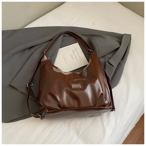 Detail view of dark brown oil wax leather tote bag with pleated crescent design and metal plate
