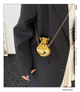 Detail of a shiny gold money bag clutch with metallic chain on a fashion model outfit