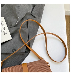 Close-up of brown woven saddle bag with leather strap on a stylish grey blazer background