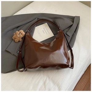 Detail of glossy chocolate brown tote bag with plush bear charm on grey blazer