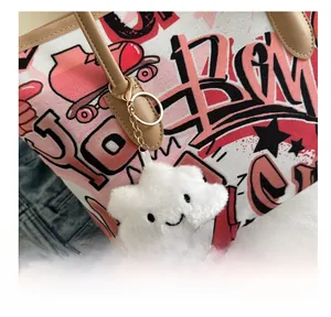 Close-up of cute white cloud plush pendant with gold metal clasp on a graffiti canvas bag