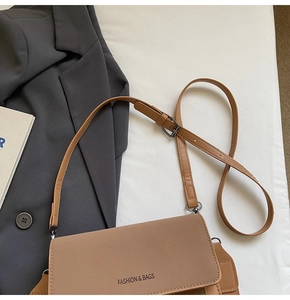 Detailed macro view of brown matte PU leather crossbody bag with wide strap on grey suit