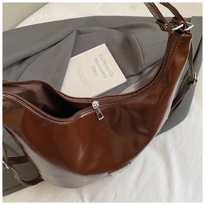 Close-up of a glossy coffee brown crescent bag with zipper on a textured white fabric