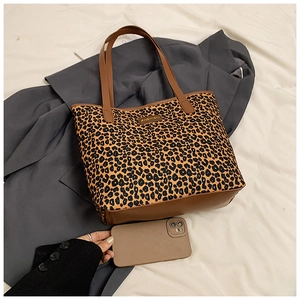 Flat lay of large leopard print tote bag with brown leather handles and gold metal logo