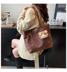 Détail du sac cabas marron avec anses en cuir et pendentif peluche dans un café chic