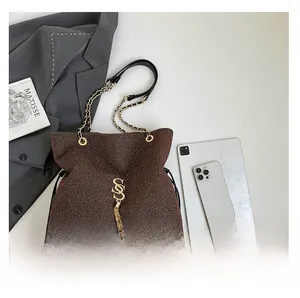 Detail of brown textured tote bag with golden S-pendant tassel and metallic chain strap