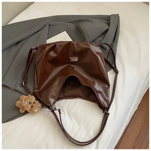 Macro detail of glossy dark brown tote bag with metallic logo and cute bear charm