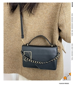 Detail van minimalistische zwarte lederen crossbodytas met gouden metalen gesp en een ketting