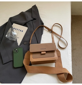 Detail of a brown leather crossbody bag featuring dual straps on an office-chic background