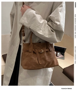 Close-up of brown suede handbag with belt buckle detail and adjustable shoulder strap