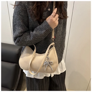 Detail of beige matte leather shoulder bag with a silver bow charm on a grey knit outfit