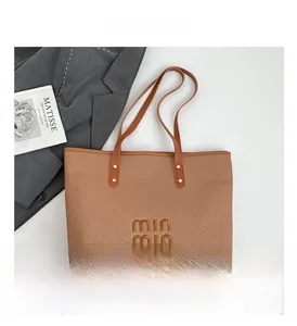 Close-up of brown woven tote bag featuring min min logo and metal rivet details