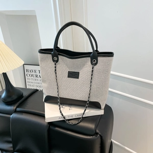 Minimalist large-capacity woven tote bag with chain strap and leather details on a bench