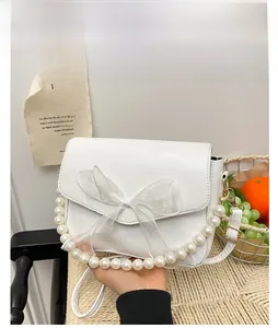 Detail of white crossbody bag featuring organza bow and elegant pearl strap handles