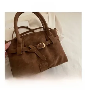 Detail view of brown faux leather handbag with grainy texture and golden buckle accents