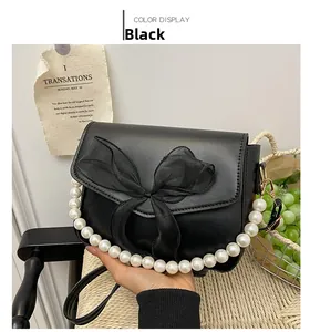 Detail of black faux leather handbag featuring a mesh bow and elegant pearl handle strap