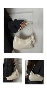Detail view of cream half-moon underarm bag with silver bow charm on a grey sweater
