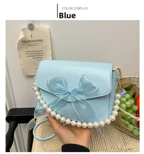 Detail of light blue shoulder bag with large mesh bow and elegant pearl handle strap
