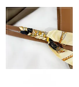 Gros plan d'un foulard en soie à imprimé chaîne enroulé sur une bandoulière en cuir