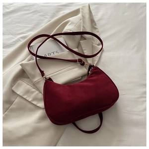 Detail of burgundy velvet hobo bag with gold hardware on a beige blazer background