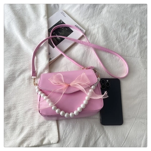 Detailed flat lay of pink mini handbag featuring mesh bow and white pearl chain