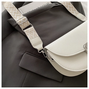 Gros plan d'un sac besace en cuir blanc avec une bandoulière tissée aux motifs beige