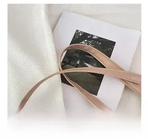 Detail van beige crossbodytas met lederen riem en gouden ketting op zijde