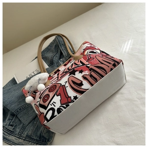 Detail of canvas tote bag with red graffiti print, brown leather handles and pompom charm