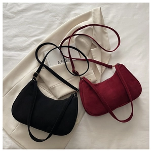 Detail of minimalist suede crescent underarm bags in black and burgundy on white fabric