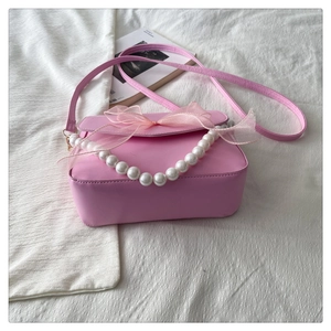 Detail of pink pearl chain bag featuring organza bow and dual shoulder straps