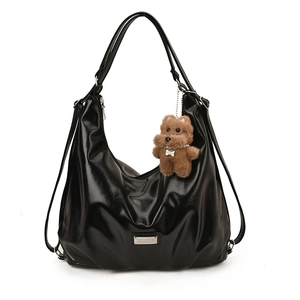 Glossy black tote bag with wrinkled texture and cute plush dog charm on white background