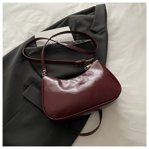 Dettaglio borsa a mezzaluna bordeaux con zip dorata su una giacca nera elegante