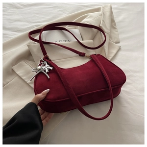 Detail of burgundy frosted leather crescent bag with silver bow charm on ivory suit