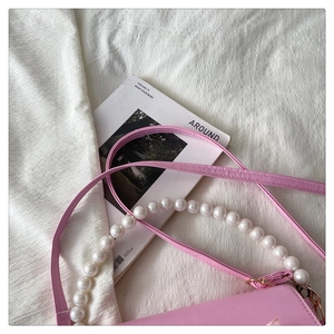 Close-up of pink crossbody bag with elegant white pearl handle and leather strap