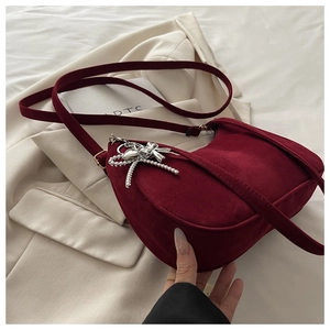 Close-up of wine red suede crescent bag with silver bow charm on a beige blazer