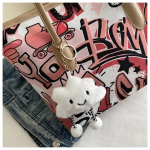 Close-up of a white plush cloud charm with a smiley face hanging on a canvas tote bag