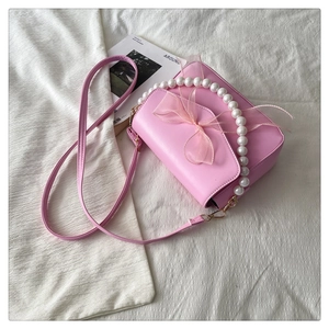 Detail of pink crossbody bag with pearl handle and mesh bow on white textured cloth