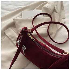 Detail of burgundy velvet handbag with golden zipper and silver rabbit pendant decor