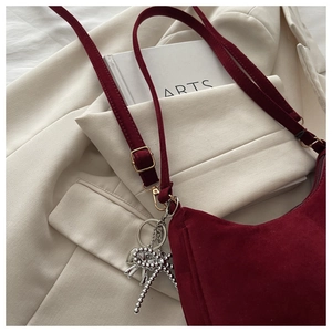 Close-up of wine red suede crossbody bag with elegant silver bow pendant detail