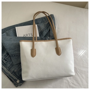 Detail of canvas tote bag with brown leather handles and smooth texture on white bedding