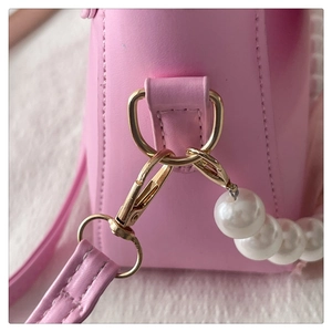 Macro shot of gold-tone metal hooks and pearl chain details on a pink leather bag