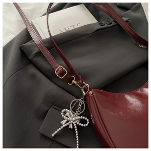 Dettaglio borsa sottobraccio bordeaux lucida con fiocco argentato su blazer grigio