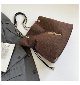 Dettaglio di una borsa a secchiello glitter marrone con catena dorata e decori a lettere
