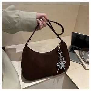 Detail of dark brown suede hobo bag with silver bow and heart charms in a lifestyle setting