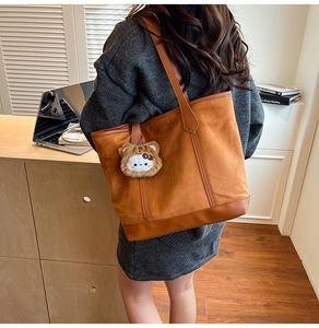 Détail d'un cabas en daim marron avec garniture en cuir et un charmant chat en peluche