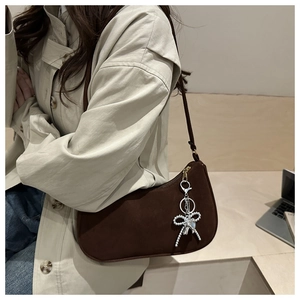 Brown suede shoulder bag with silver bow charm detail on a beige trench coat