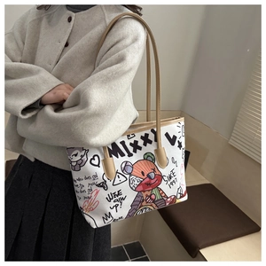 Close-up of a white canvas tote bag with comic bear graffiti and brown leather straps